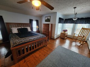 A bedroom with a wooden bed, a dresser, a rocking chair, and a window with curtains.