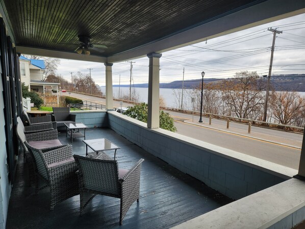 A covered outdoor seating area with wicker furniture and a view of a road and lake.