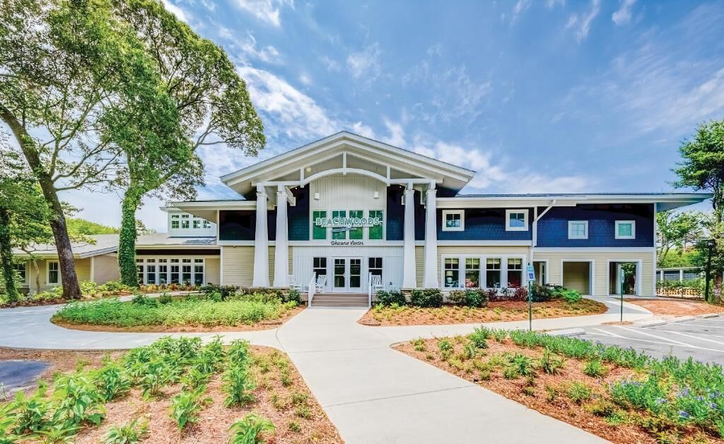 A two-story building with a central entrance, surrounded by landscaped gardens and a clear sky.