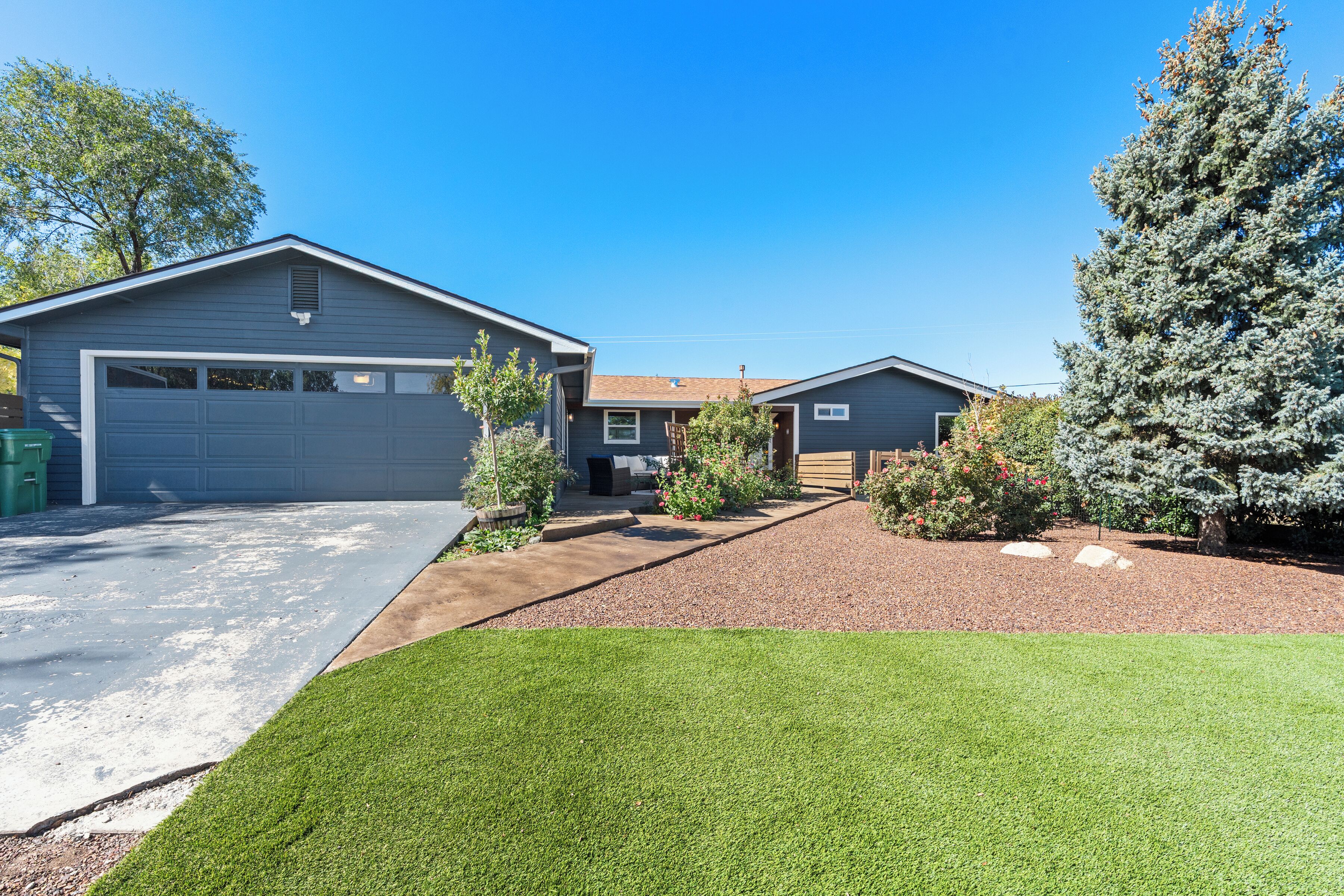 A residential property with a garage, a well-maintained lawn, and a large evergreen tree.