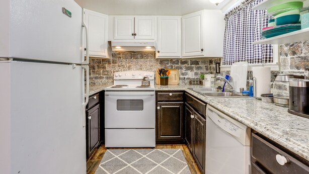 A compact kitchen with white cabinets, a white stove, and a dishwasher. - Cozy Wasilla Apartment ~ 2 Mi to Downtown! (Wasilla)