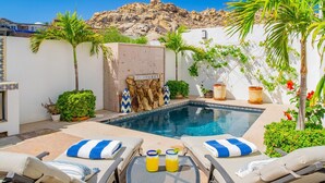 A pool area with lounge chairs, a small pool, and a rocky hill in the background.