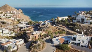 A coastal town with white buildings, a beach, and a mountain in the background.