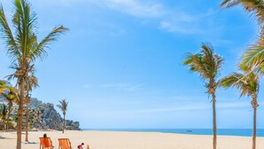 A beach with palm trees, a sandy shore, and a clear blue sky.
