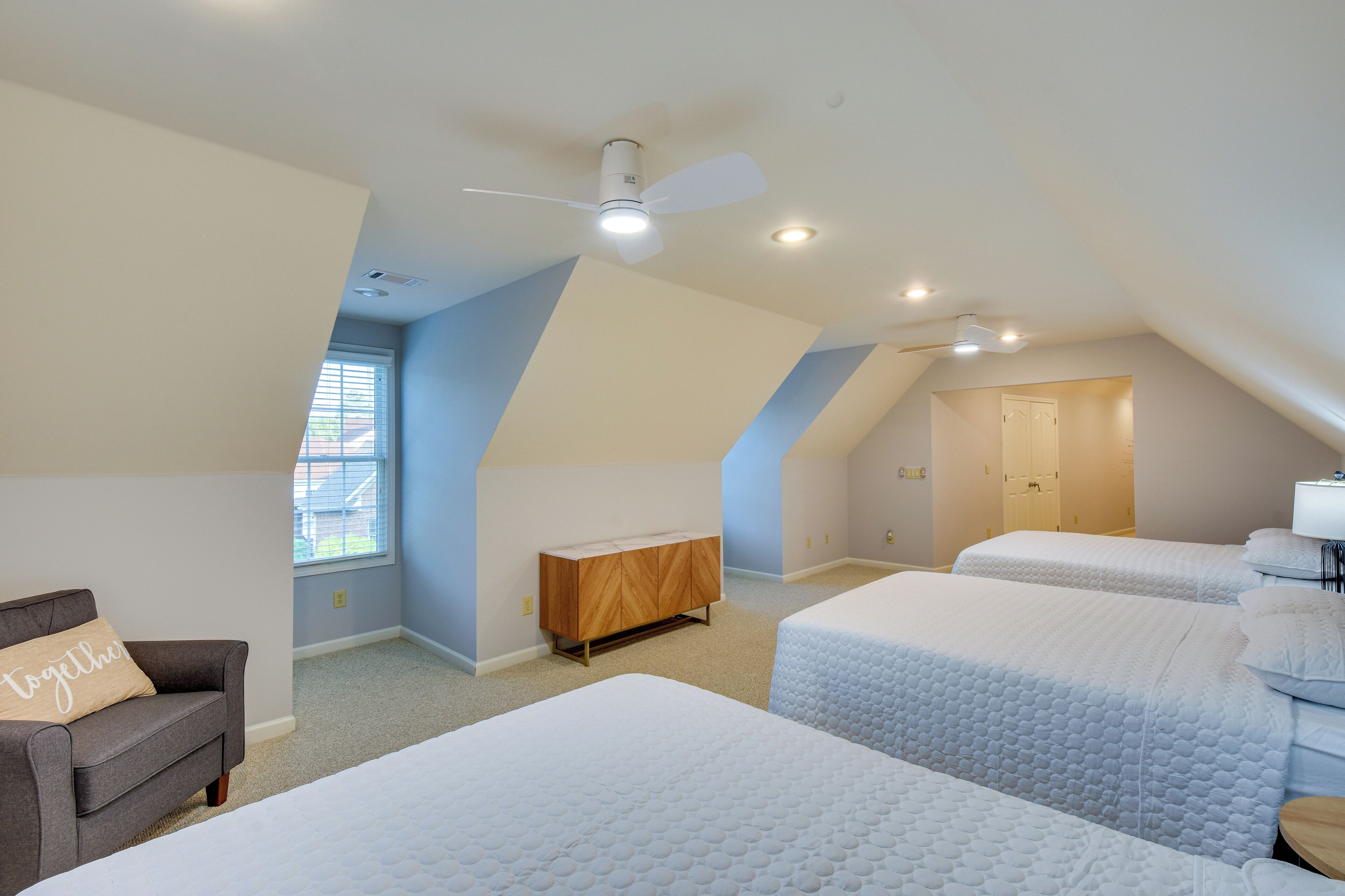 A bedroom with two beds, a wooden cabinet, a gray sofa, and a ceiling fan.