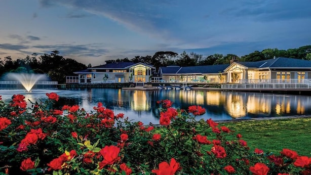 A waterfront hotel with a reflective pool, a fountain, and a row of red flowers in the foreground.