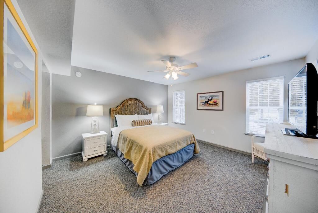 A bedroom with a bed, bedside tables, a ceiling fan, and a desk with a chair.