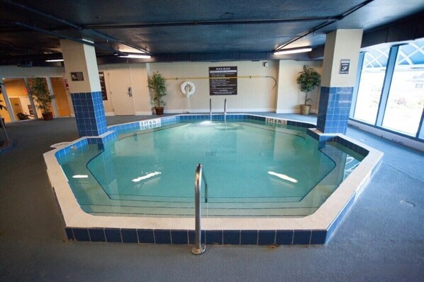 An indoor swimming pool with a tiled edge, a lifeguard stand, and a sign indicating pool rules.
