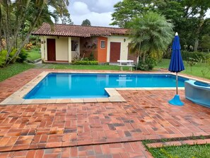 Relax by the pool surrounded by lush greenery and a brick patio.