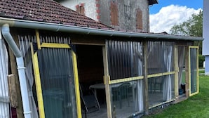 A house with a covered outdoor area, a visible door, and a window. - Can Appart 1 à 8 Pers (Granges-Aumontzey)