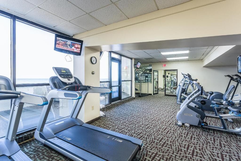 A gym with treadmills, elliptical machines, and a TV screen.