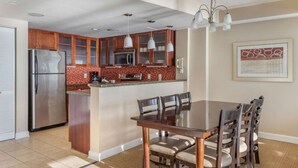 Een moderne keuken met een centraal eiland, roestvrijstalen apparatuur en een eethoek met een tafel en stoelen.