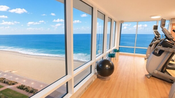 Een sportschool met trainingsapparatuur en een groot raam met uitzicht op een strand.