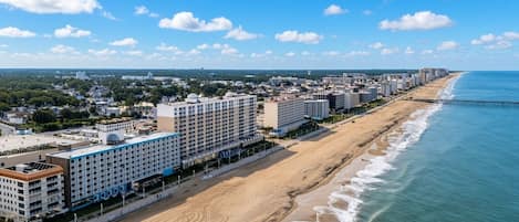 Un hotel frente al mar con varios pisos, un paseo marítimo y un muelle que se adentra en el océano.
