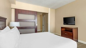 Een hotelkamer met een groot bed, een houten dressoir, een televisie en een deur naar een andere kamer.