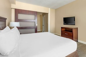 Een hotelkamer met een groot bed, een houten dressoir, een televisie en een deur naar een andere kamer.