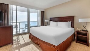 A hotel room with a large bed, a desk, a chair, and a view of the ocean through the balcony doors. - Diamond Resorts Ocean Beach Club - 1 Bed Acc Roll-in Shower Oceanfront (Virginia Beach)