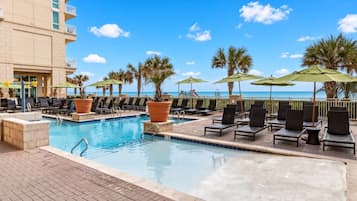 Un espace piscine avec des chaises longues et des parasols, donnant sur une plage.