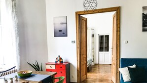 A room with a dining table, chairs, a red chest of drawers, a blue sofa, and a wooden floor. - Bonerowska 3/48 (Kraków)