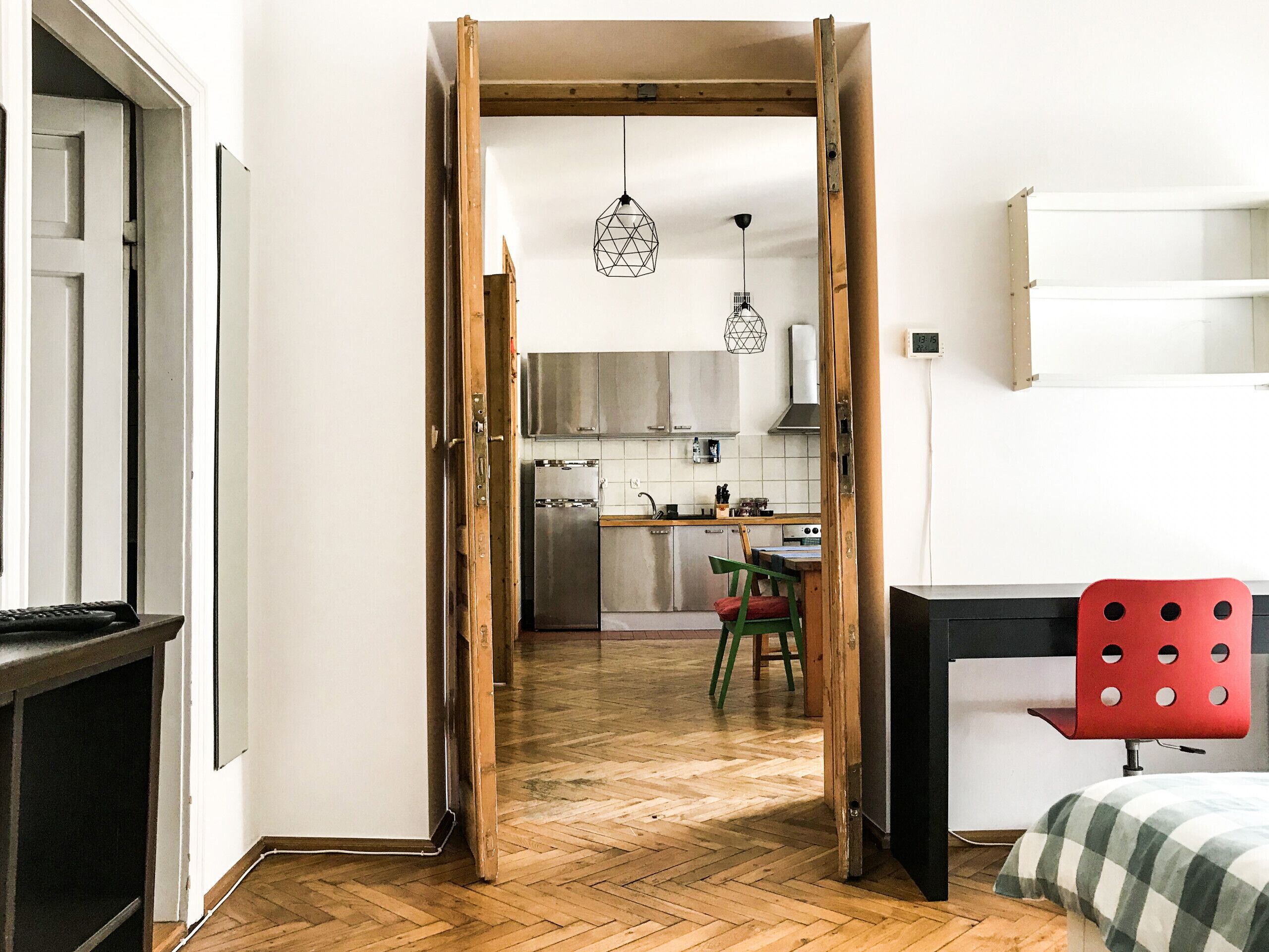 Un corridoio stretto che porta a una cucina con una porta di legno, una sedia rossa e un letto con coperta a quadri.