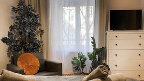 A hotel room with a sofa, a large potted plant, a wooden side table, a TV, and a dresser. - Apartment for 4 guests, Wawel & Old Town Krakow II, św. Gertrudy (Kraków)