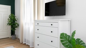 A room with a white dresser, a flat-screen TV mounted above it, a potted plant, and a window with sheer curtains. - Apartment for couples - Wawel & Old Town Krakow, św. Gertrudy (Kraków)