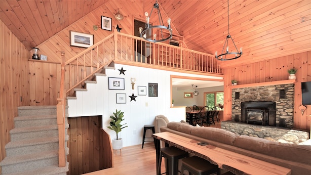 Un intérieur en bois avec un escalier, une chemin ée en pierre, un banc en bois et un coin repas.