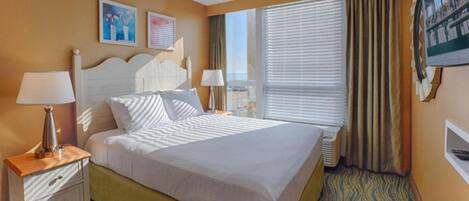 A hotel room with a bed, two bedside tables, a window with curtains, and wall-mounted artwork.