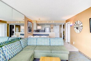 A modern living room with a sectional sofa, a small table, and a kitchen in the background.