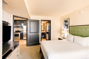 A hotel room with a bed, a television, a kitchenette, and a bathroom.