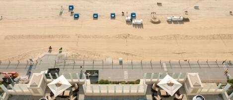 Vista aérea de un hotel frente a la playa con zona de piscina, sillas de descanso y vistas al océano.