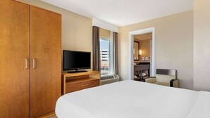 Habitación de hotel con una cama grande, un televisor sobre un soporte de madera, un baño con espejo y lavamanos, y vistas al exterior a través de la ventana.