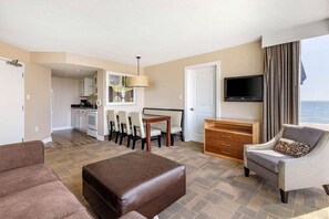 Habitación de hotel con sala de estar, kitchenette, televisor de pantalla plana, sofá, reposapiés marrón y vista al mar.