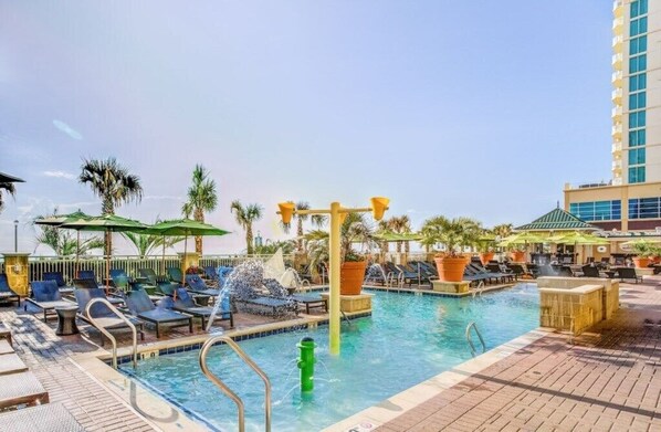 Ein Poolbereich mit Liegestühlen, Sonnenschirmen und einer Wasserspielsäule.