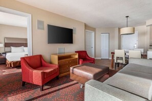 A hotel room with a bed, a TV, a red armchair, a brown ottoman, and a grey sofa. - Diamond Resorts Ocean Beach Club - 2 Bed Lock-off Access. Oceanfront (Virginia Beach)