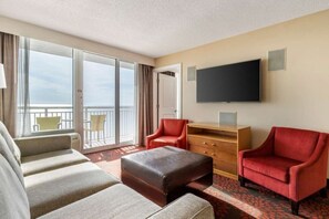 Une chambre d’hôtel dotée d’une grande fenêtre, d’un téléviseur à écran plat, d’un canapé, de deux fauteuils, d’une commode en bois et d’un balcon avec une chaise.