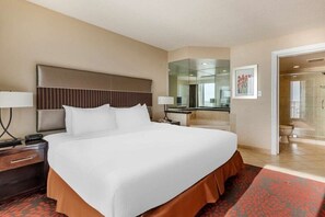 Ein Hotelzimmer mit einem großen Bett, einem Nachttisch, einem Schreibtisch, einem Spiegel und einer Dusche.