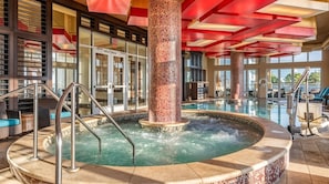 Un espace dédié à un bain à remous, doté d’un sol carrelé, de rampes en métal et d’une colonne centrale ornée d’un motif en mosaïque.