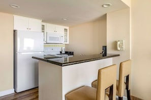 Une cuisine compacte avec des meubles blancs, un four à micro-ondes, une cuisinière et un petit îlot central doté de chaises.