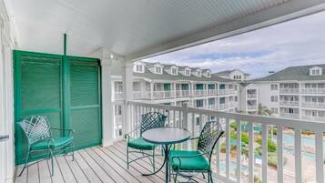 A covered outdoor area with a wooden deck, green chairs, and a round table.