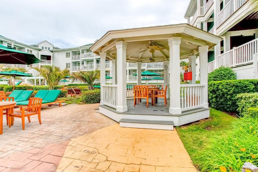 A covered outdoor seating area with a table and chairs, surrounded by greenery and a poolside lounge.