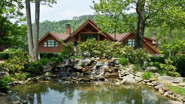 A lodge with a pond, surrounded by trees and a waterfall.
