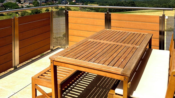 A wooden deck with a table and chairs, overlooking a rural landscape with fields and wind turbines. - Quietly located apartment on the pond on the upper floor with balcony (Nideggen)