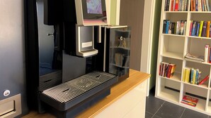 A coffee machine with a digital display, a bookshelf with books, and a door in a room. - Quietly located apartment on the pond on the upper floor with balcony (Nideggen)