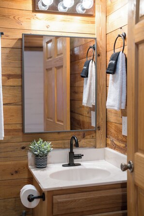 A wooden bathroom with a sink, mirror, towel rack, and a potted plant. - Red Feather Cabins 250 (Boone)