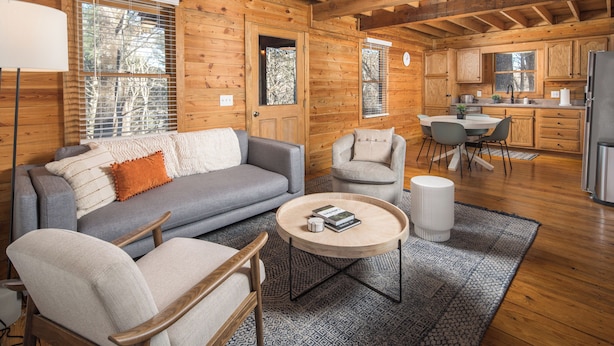 Een gezellig interieur van een vakantiehuisje, met een zithoek met een bank, stoelen, een salontafel en een keuken met houten kastjes en een koelkast.