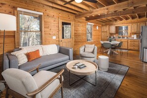 A cozy cabin interior with a living area featuring a sofa, chairs, a coffee table, and a kitchen with wooden cabinets and a refrigerator. - Red Feather Cabins 250 (Boone)
