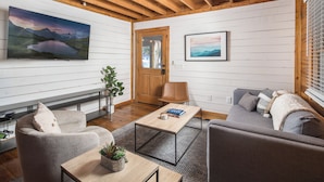 Een moderne woonkamer met een houten plafond, een flatscreen televisie, een bank, een salontafel en een deur.