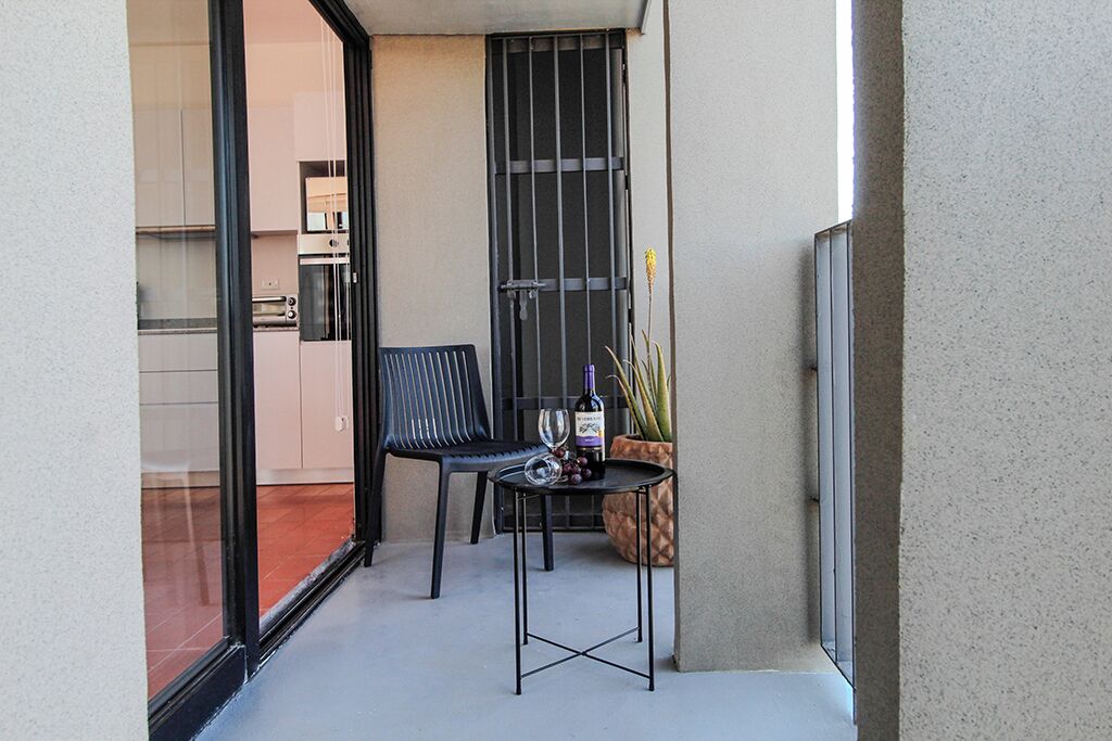 A small balcony with a chair, a table, a potted plant, and a bottle of wine.