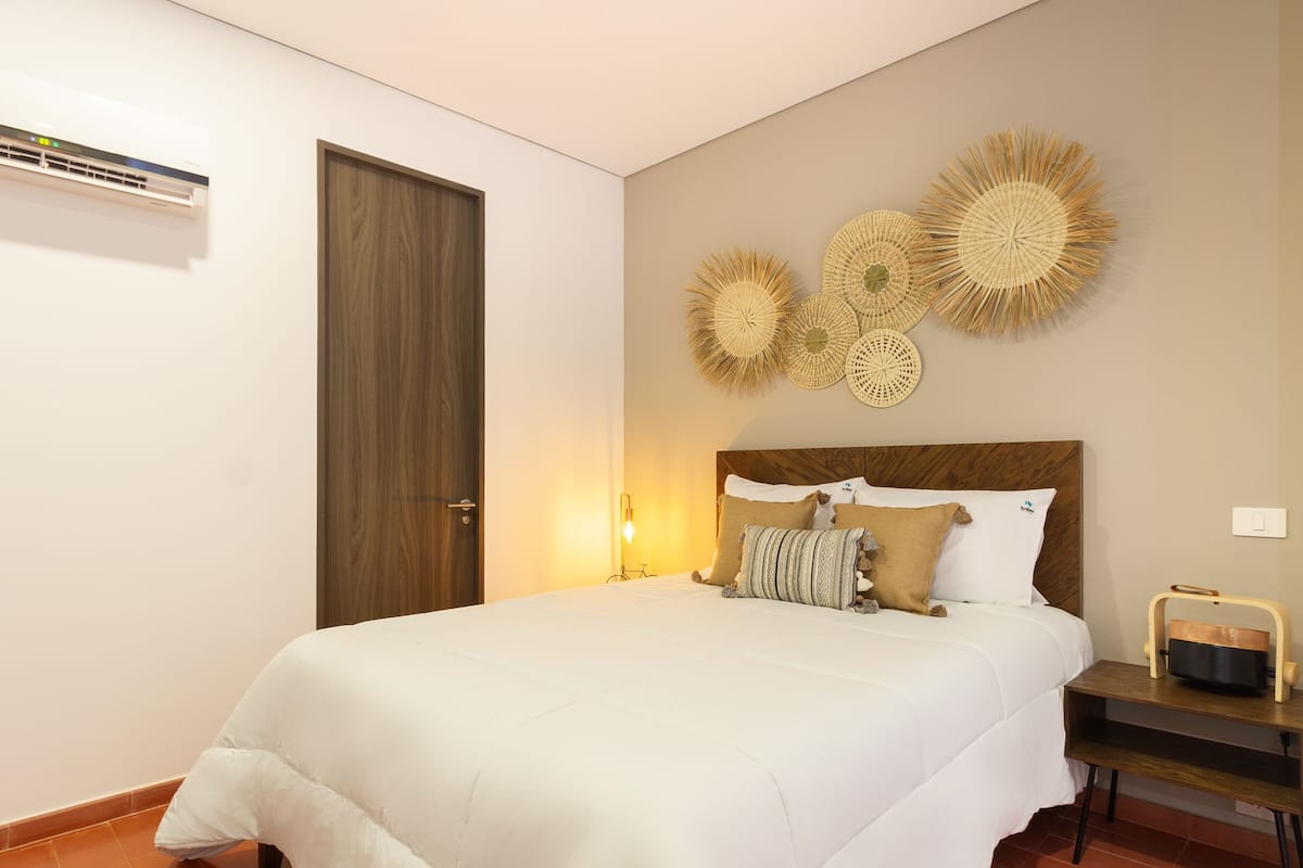 Una cama bien tendida con ropa blanca, cabecera de madera y decoración mural.